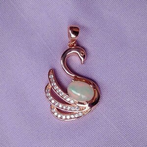May include: A rose gold swan pendant with a white opal gemstone in the center. The swan is adorned with small clear cubic zirconia stones.