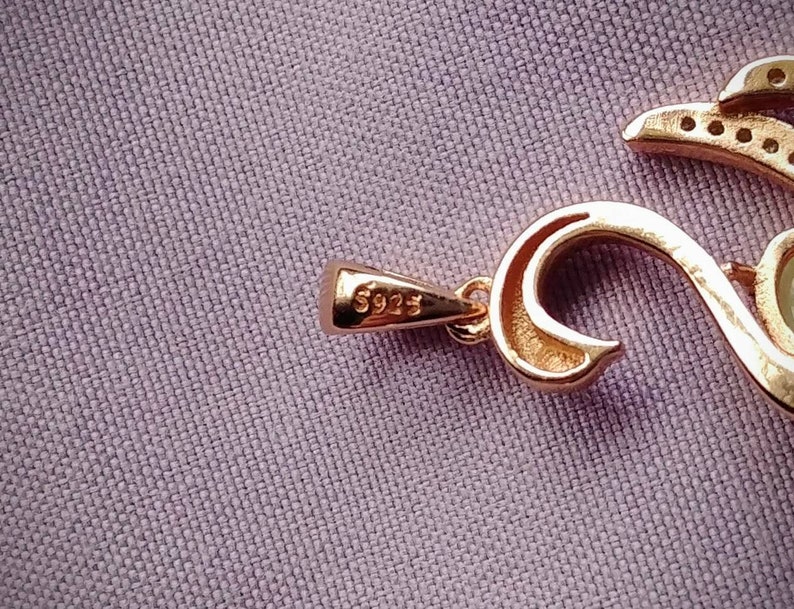 May include: A gold pendant necklace with a detailed design featuring a heart shape and a small pearl. The pendant is marked with the number "5925".