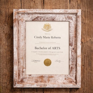 May include: A framed Bachelor of Arts diploma featuring the name Cindy Marie Roberts. The frame is white with a distressed finish, set against a rustic wooden background. The diploma includes a gold seal and is decorated with a floral arrangement.