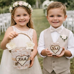 May include: A young girl holds a white wooden flower basket with a jute handle and floral accents. The basket has a heart with "H&A" and an arrow. A young boy holds a wooden hexagon box with "H&A" in a heart. Both are dressed for a wedding.