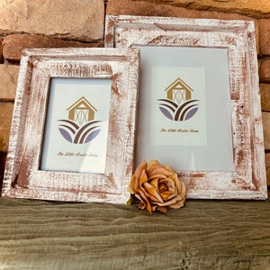 May include: Two rustic white wood picture frames with a farmhouse style design. The smaller frame is in front of the larger frame. Both frames have a white background with a brown barn and the text "The Little Rustic Farm".