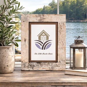 May include: A framed print with a rustic birch bark frame. The print features a barn illustration in brown and tan, with purple and brown accents, and the text "The Little Rustic Farm". A candle lantern and a vase with greenery are nearby.