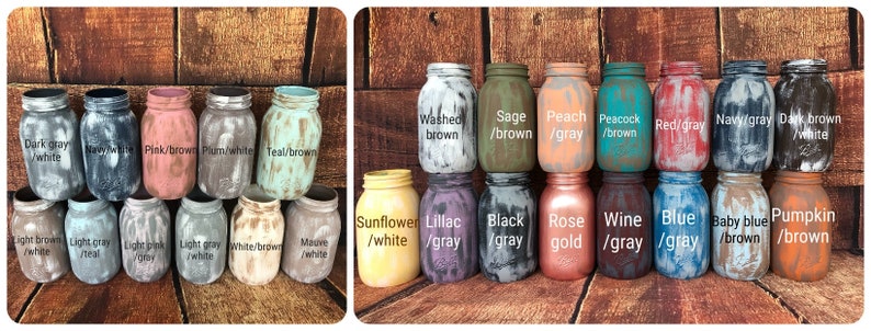 May include: A collection of painted mason jars in various colors, including dark gray, navy, pink, teal, and sunflower. Each jar has a distressed, rustic finish. The jars are labeled with color combinations like "Washed brown" and "Rose gold."