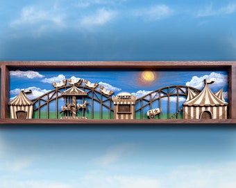 May include: A wooden framed wall art piece depicting a miniature carnival scene with a carousel, roller coaster, ticket booth, and two striped tents. The scene is painted on a blue background with white clouds and a yellow sun.