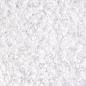 May include: A close-up image of a large quantity of small, white, opaque glass seed beads. The beads are round and have a slight iridescent sheen.