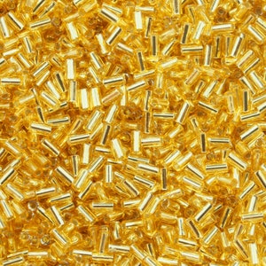 May include: A close-up image of a large quantity of gold-colored glass beads. The beads are small and cylindrical in shape.