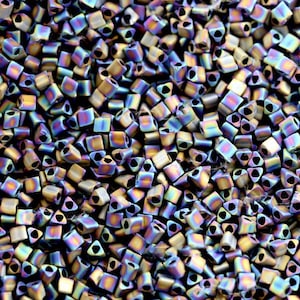 May include: Close-up of a pile of iridescent square beads. The beads have a metallic sheen with colors shifting from gold to blue and purple. Each bead has a triangular hole. These beads are ideal for jewelry making and crafting.