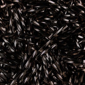 May include: A close-up image of a pile of black, shiny, rectangular beads. The beads are arranged in a random pattern, creating a textured and abstract look.