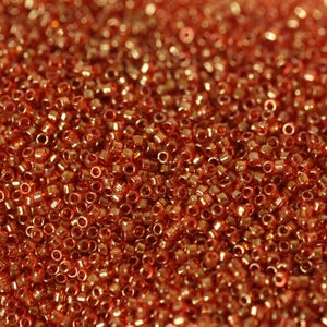 May include: A close-up image of a large quantity of small, round, orange-colored glass beads. The beads have a metallic sheen and are arranged in a random pattern.