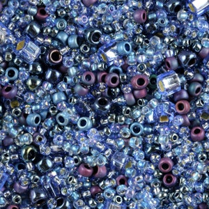 May include: A close-up of a variety of blue and purple glass beads. The beads are of different shapes and sizes, and some have iridescent finishes.