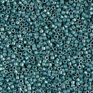Può includere: Una vista ravvicinata di una grande quantità di perline di semi di colore turchese. Le perline sono piccole e rotonde con un foro al centro. Sono disposte in uno schema casuale.