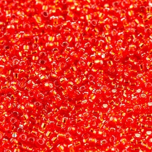 May include: A close-up image of a large quantity of small, red glass beads. The beads have a shiny, iridescent finish.