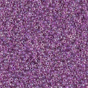 May include: A close-up image of a large quantity of small, round, iridescent purple glass beads. The beads have a clear glass base with a purple iridescent coating.
