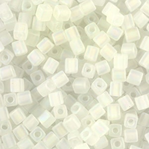 May include: A close-up of a pile of small, white, square beads with a subtle iridescent sheen. The beads are opaque and have a smooth, polished finish.
