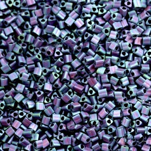 May include: A close-up of a pile of small, iridescent, triangular-shaped beads. The beads are a mix of purple, blue, and green.