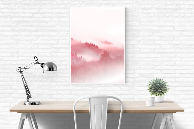 May include: A digital art print of a foggy forest scene in shades of pink and white. The print is framed and hanging on a white brick wall above a desk with a lamp and a plant.