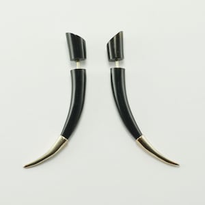 May include: A pair of black horn-shaped earrings with gold-coloured tips. The earrings have a post and backing design. The earrings are set against a white background.