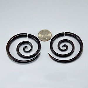 May include: A pair of dark brown wooden spiral earrings. The earrings are about the size of a US quarter.