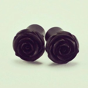 May include: A pair of black wooden ear gauges with a rose design.