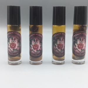 Könnte beinhalten: Vier Glasflaschen mit schwarzen Roll-on-Deckeln und Etiketten mit der Aufschrift "Handfasting" mit einem Rosen- und Zwei-Vogel-Design. Die Flaschen enthalten eine klare Flüssigkeit.