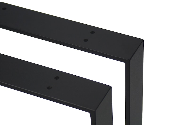 Op de afbeelding: Close-up van twee zwarte metalen tafelpoten. Elke poot heeft een rechthoekige vorm met een haakse hoek en voorgeboorde gaten voor montage. De poten zijn ontworpen voor meubelconstructie.
