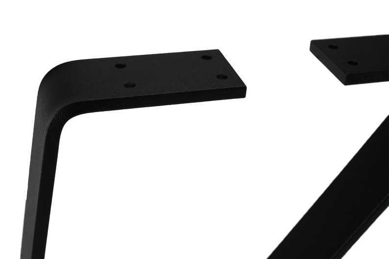 May include: Close-up of black metal table legs. The legs have a modern, angled design with a rectangular mounting plate. The legs are made of solid metal and have a matte finish. The mounting plates have pre-drilled holes for easy installation.