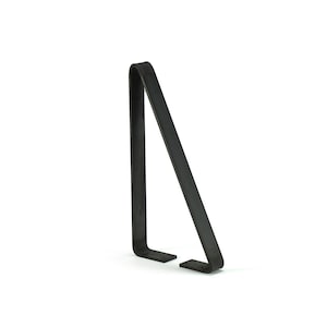 Puede incluir: Un soporte de metal negro con un dise&ntilde;o en &aacute;ngulo recto. El soporte tiene una base plana con dos peque&ntilde;os pies rectangulares y una parte superior curvada. El objeto est&aacute; sobre un fondo blanco.