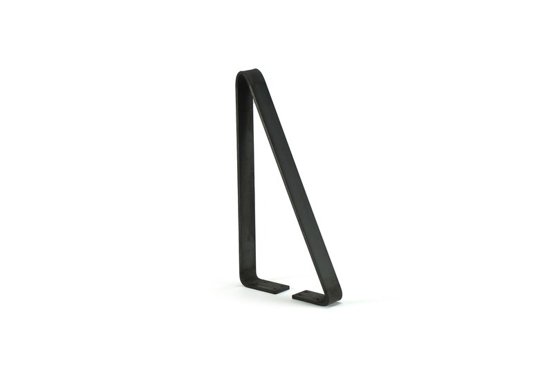 Puede incluir: Un soporte de metal negro con un dise&ntilde;o en &aacute;ngulo recto. El soporte tiene una base plana con dos peque&ntilde;os pies rectangulares y una parte superior curvada. El objeto est&aacute; sobre un fondo blanco.