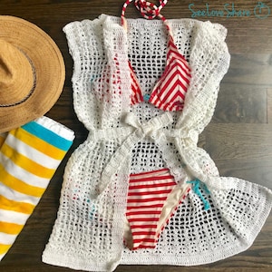 May include: White crochet cover-up with a red and white striped bikini top and bottom. The cover-up has a tie at the waist and is made of a lightweight, airy fabric.
