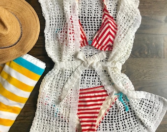 May include: White crochet cover-up with a red and white striped bikini top and bottom. The cover-up has a tie at the waist and is made of a lightweight, airy fabric.