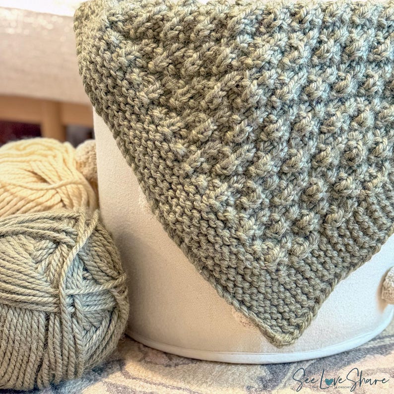 May include: A sage green crocheted fabric with a textured, raised stitch pattern draped over a white cylindrical container, accompanied by a ball of sage green yarn and a ball of cream-coloured yarn, with the text See Love Share visible.