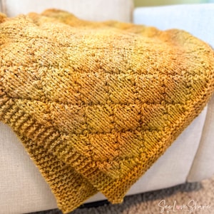May include: A knitted throw blanket in a gradient of yellow and orange hues. The blanket is made with a textured stitch pattern and has a soft, cozy feel.