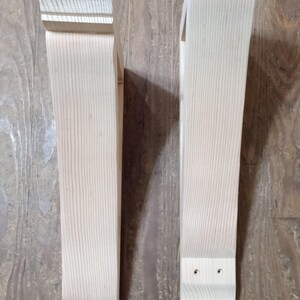 May include: Two unfinished wooden corbels with a light, natural wood grain. Each corbel has a decorative top and bottom, with a rectangular body. The corbels are designed for structural support and add a decorative element.
