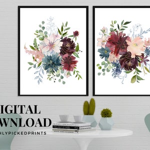 May include: Two framed floral art prints. Each print features a watercolor bouquet with burgundy, blue, and blush-colored flowers, accented with green foliage and gold detailing. The prints are set against a white background.