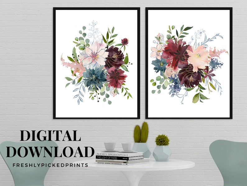 May include: Two framed floral art prints. Each print features a watercolor bouquet with burgundy, blue, and blush-colored flowers, accented with green foliage and gold detailing. The prints are set against a white background.