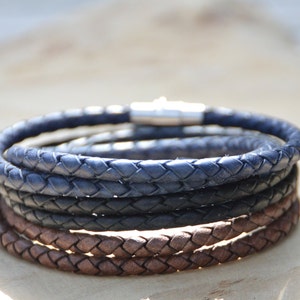 Op de afbeelding: Een stapel van vier gevlochten leren armbanden in donkerbruin en donkerblauw. De armbanden hebben een zilveren magneetsluiting.
