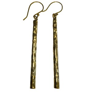 May include: A pair of gold hammered bar earrings with a textured finish. The earrings are long and slender, with a simple hook closure.