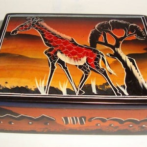 May include: A wooden box with a black and white painted giraffe on a sunset background. The box has a dark blue trim and a red and orange bottom with a geometric design.