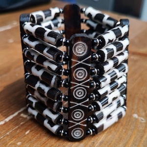 May include: A black and white patterned wooden bracelet with black beads. The bracelet is made of multiple layers of wood and beads.