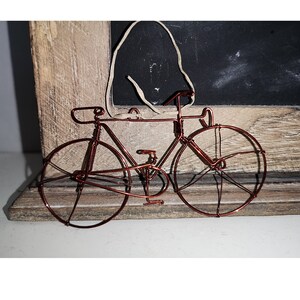 May include: A copper wire bicycle sculpture with two wheels, a handlebar, and a seat. The sculpture is on a wooden surface.