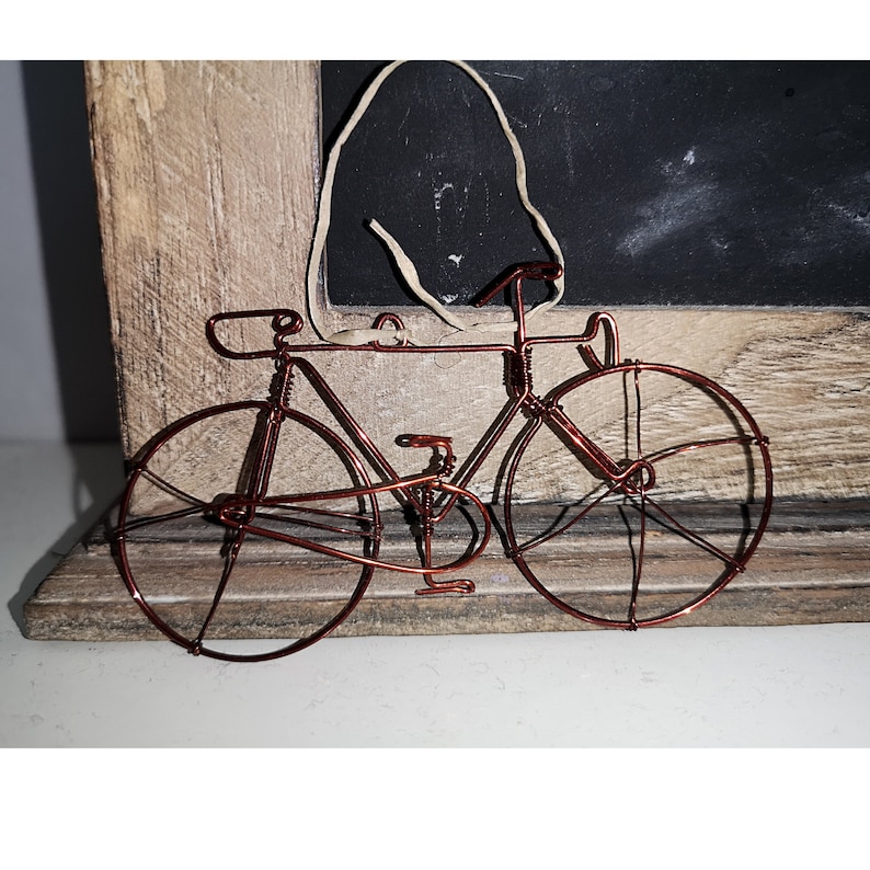 May include: A copper wire bicycle sculpture with two wheels, a handlebar, and a seat. The sculpture is on a wooden surface.