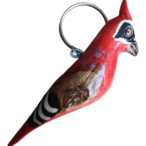 May include: A red wooden bird keyring with black and white stripes and a silver ring. The bird has a brown and white painted design on its chest.