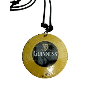 May include: A gold-coloured round pendant with a black Guinness logo and the text "ESTD 1759" hanging from a black cord.
