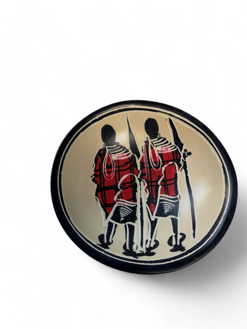 May include: A small, round wooden bowl with a black rim. The bowl is decorated with a hand-painted design of three people in red and black clothing. The people are standing in a line, and they are holding spears.