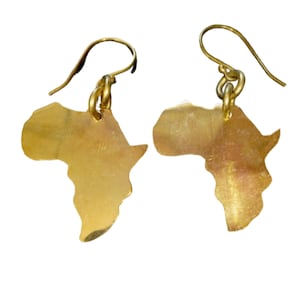 Może przedstawiać: Para złotych kolczyków w kształcie kontynentu afrykańskiego. Kolczyki są wykonane z metalu i mają prosty design.