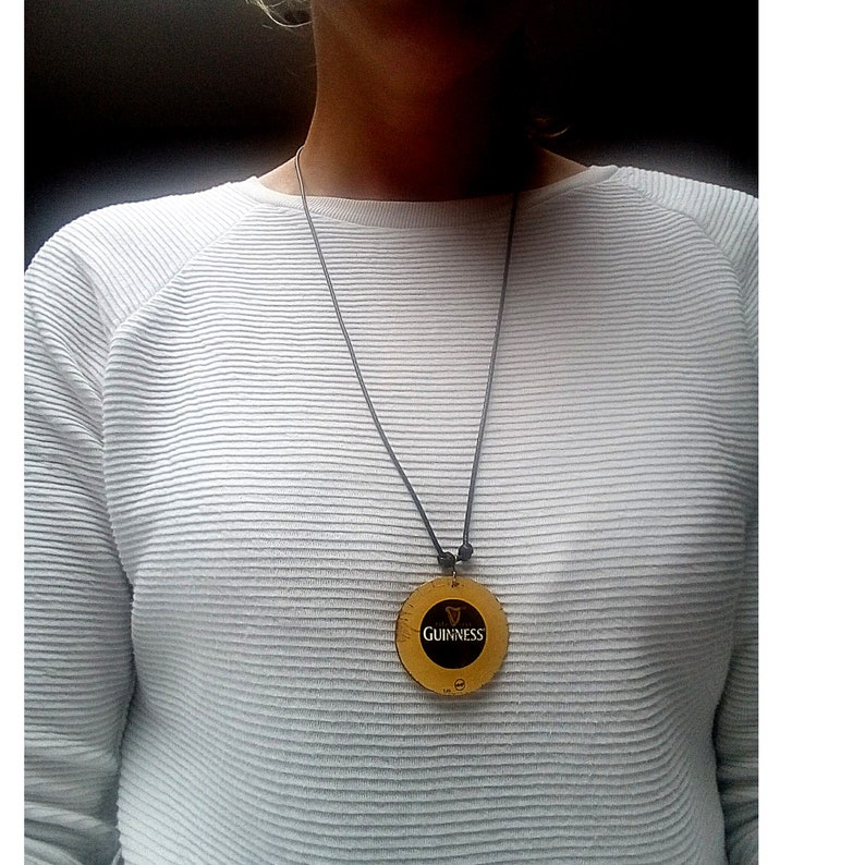 May include: A black cord necklace with a round, gold-coloured pendant featuring the Guinness logo.