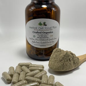 Peut inclure: Un flacon en verre brun &eacute;tiquet&eacute; Herbal Cell Food Plus contenant des g&eacute;lules, avec une cuill&egrave;re en bois contenant un tas de poudre brun clair et plusieurs g&eacute;lules &eacute;parpill&eacute;es devant, le tout pr&eacute;sentant un aspect brun clair et terreux.