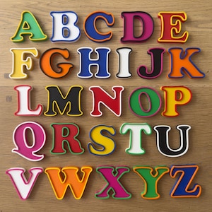 Puede incluir: Un conjunto completo de veintiséis letras del alfabeto, de la A a la Z. Cada letra está representada en una fuente gruesa y llamativa con una cara de color distintivo y un contorno contrastante. Las letras presentan una variedad de colores brillantes, incluyendo rojo, azul, verde, amarillo, naranja, rosa, negro y blanco.