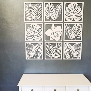 May include: A set of nine white wall decor panels featuring various tropical leaf designs. The panels are arranged in a 3x3 grid and are made of a lightweight material.