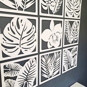 May include: Nine white square wall decor panels with cut-out tropical leaf designs. The panels feature various leaf shapes, including monstera, palm, and orchid.